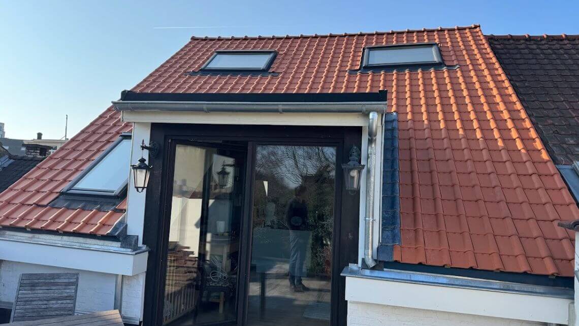 Toiture rénovée en tuiles neuves rouges avec fenêtres de toit et verrière donnant sur une terrasse.